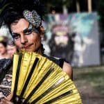 The emotional expression of the person in vintage style attire and bold makeup, holding a yellow fan.