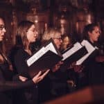 The the vintage-style choir women passionately sing with sheet music in a timeless, emotional moment.