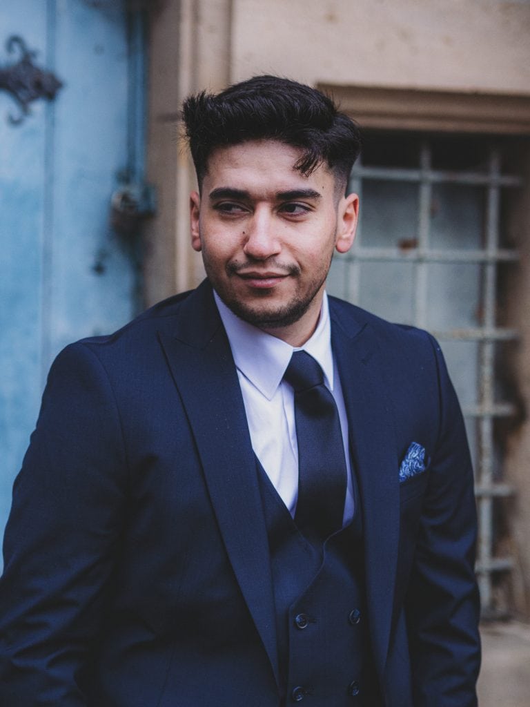 A man in a vintage navy suit with a tie, standing outdoors, showcasing timeless elegance and confident charm in a retro-inspired setting.