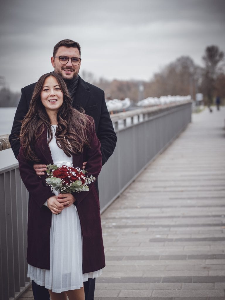The image captures a romantic vintage scene of a couple on a bridge, dressed elegantly, with a bouquet, evoking warmth and timeless affection.