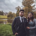 The vintage-style couple stands close together in a lush park with autumn foliage, radiating warmth.